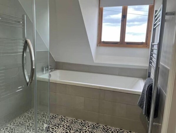 Un baño moderno con cabina de ducha de vidrio, una bañera independiente y baldosas de suelo estampadas.