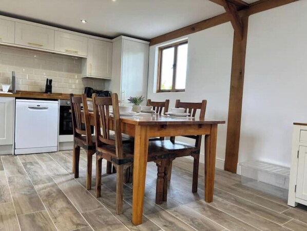Una cocina con armarios blancos, una mesa de comedor de madera con sillas y una ventana.