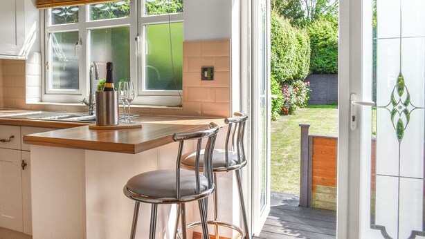 A modern kitchen with a large window, a wine bottle, and two bar stools. - 2 bedroom accommodation in Whitby (Whitby)