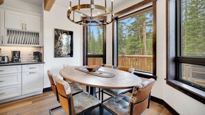 Una cocina moderna con armarios blancos, una mesa de comedor de madera y un ventanal con vistas a un bosque.