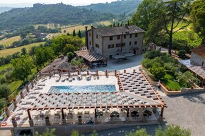 A rooftop pool area with lounge chairs and a pergola, surrounded by a stone building and lush greenery. - Agriturismo Beata Vanna (Fabro)
