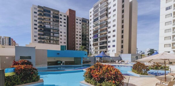 A hotel with a swimming pool, outdoor seating, and high-rise buildings in the background.