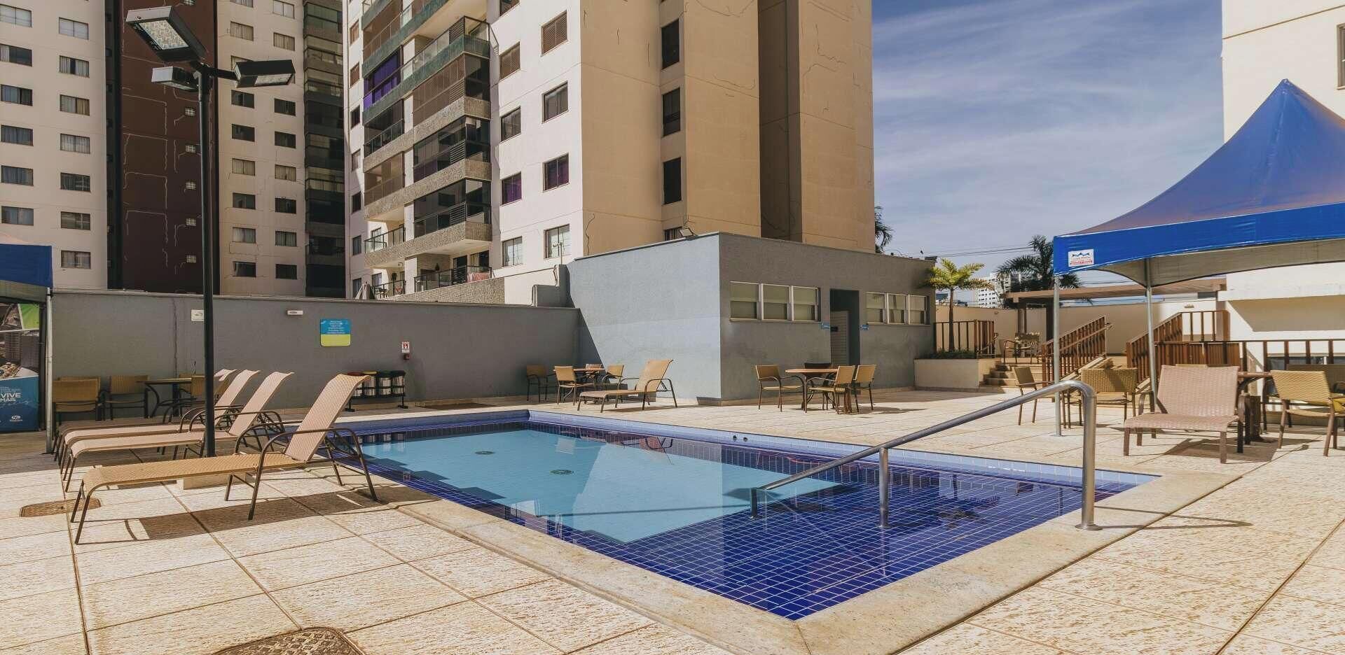A swimming pool with lounge chairs and a covered area, surrounded by high-rise buildings.