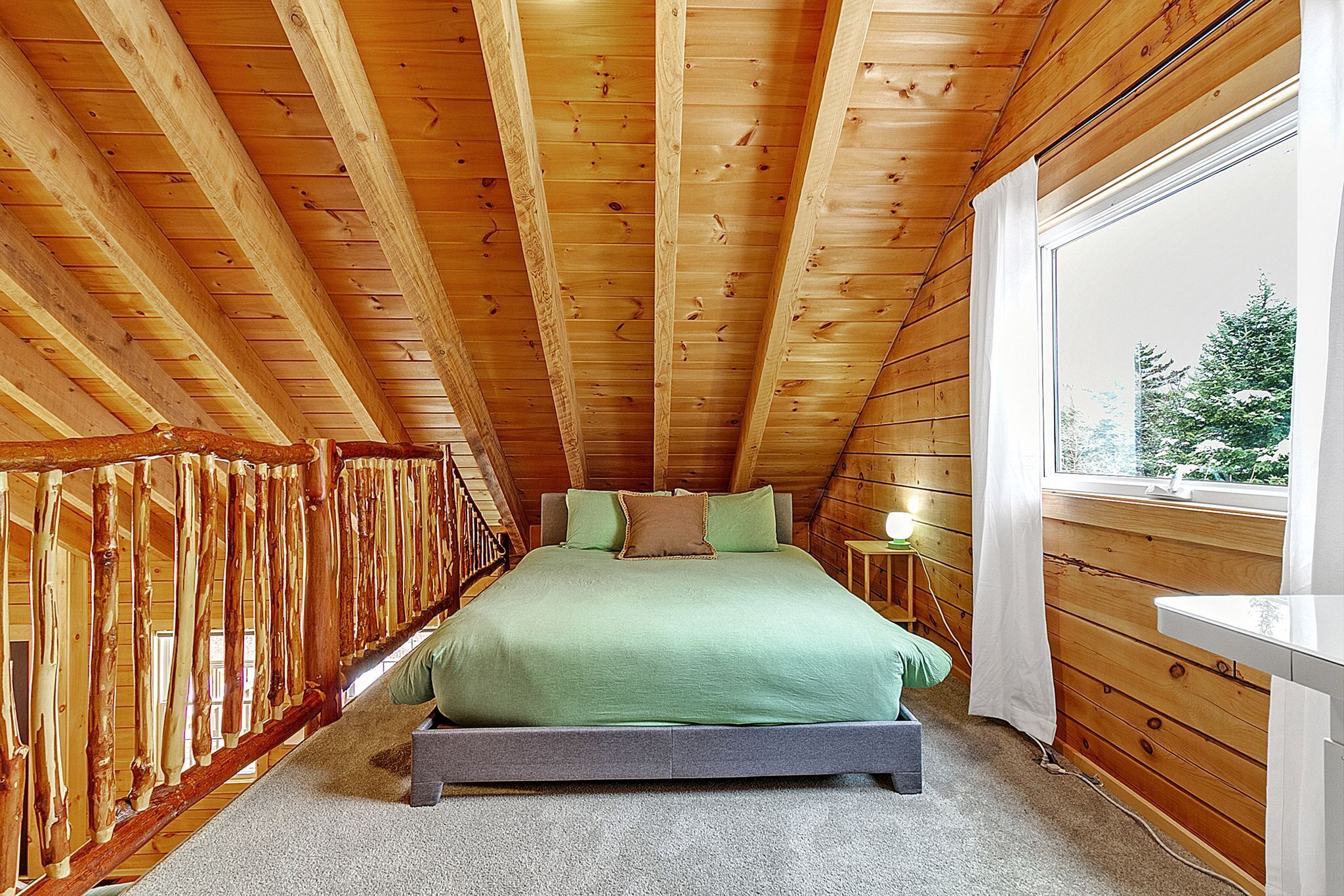 A wooden-paneled room with a bed, a window, and a wooden railing.