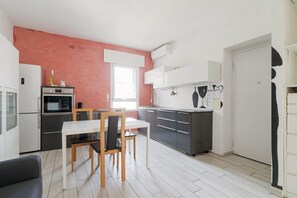 A modern kitchen with a dining area, white cabinets, and a red accent wall.