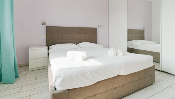 Una habitación de hotel moderna con una cama grande, una mesita de noche, un espejo y una cortina color aguamarina.