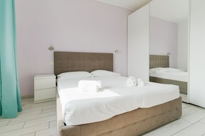 Una habitación de hotel moderna con una cama grande, una mesita de noche, un espejo y una cortina color aguamarina.