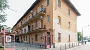 Un edificio de varios pisos con balcones, una entrada protegida por una reja y un letrero de 'prohibido estacionar'.