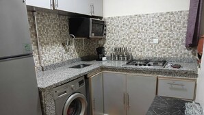 A compact kitchen with a washing machine, a microwave, and a sink. - Rest Appar (Agadir)