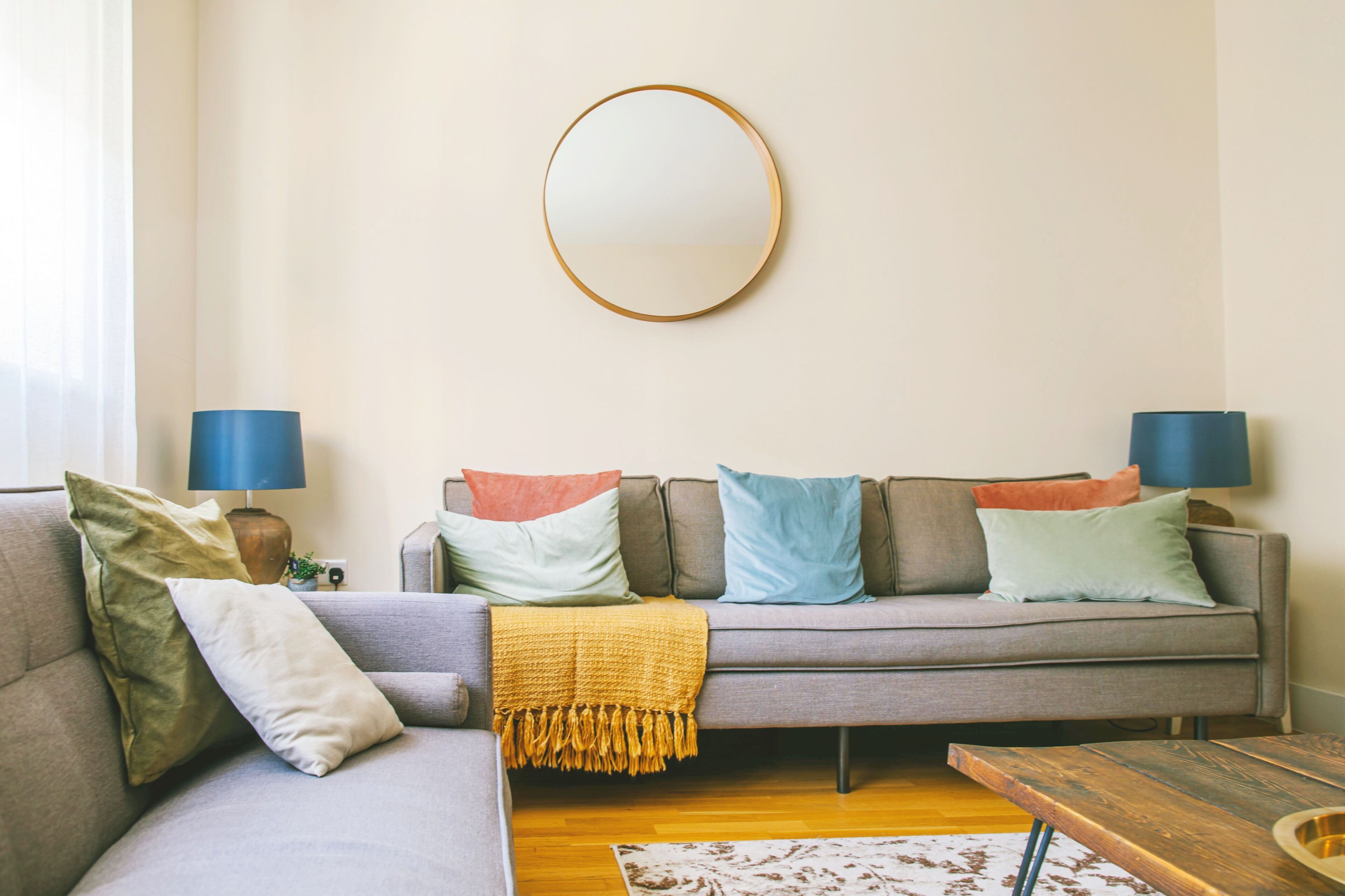 A living room with a grey sofa, a round mirror, and two lamps.