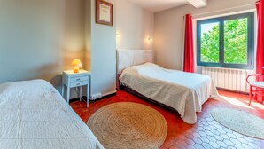 A room with two beds, a small table with a lamp, a framed certificate on the wall, and a window with red curtains. - Apartment 'Gîte Coté Mûrier' with Shared Pool, Private Terrace and Wi-Fi (Rasteau)