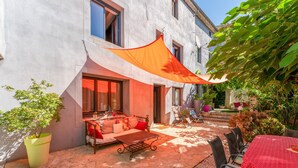 A patio with a sofa, table, and chairs, a potted plant, and a building with windows and a door. - Apartment 'Gîte Coté Mûrier' with Shared Pool, Private Terrace and Wi-Fi (Rasteau)