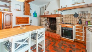 A kitchen with a stone fireplace, wooden cabinets, a wooden table, and a white chair. - Apartment 'Gîte Coté Mûrier' with Shared Pool, Private Terrace and Wi-Fi (Rasteau)