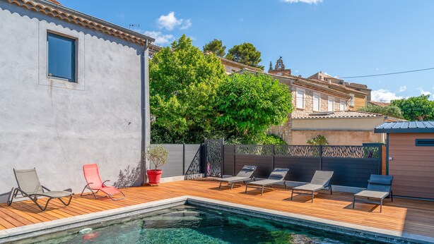 A swimming pool with lounge chairs, a wooden deck, and a building with a tiled roof. - Apartment 'Gîte Coté Mûrier' with Shared Pool, Private Terrace and Wi-Fi (Rasteau)
