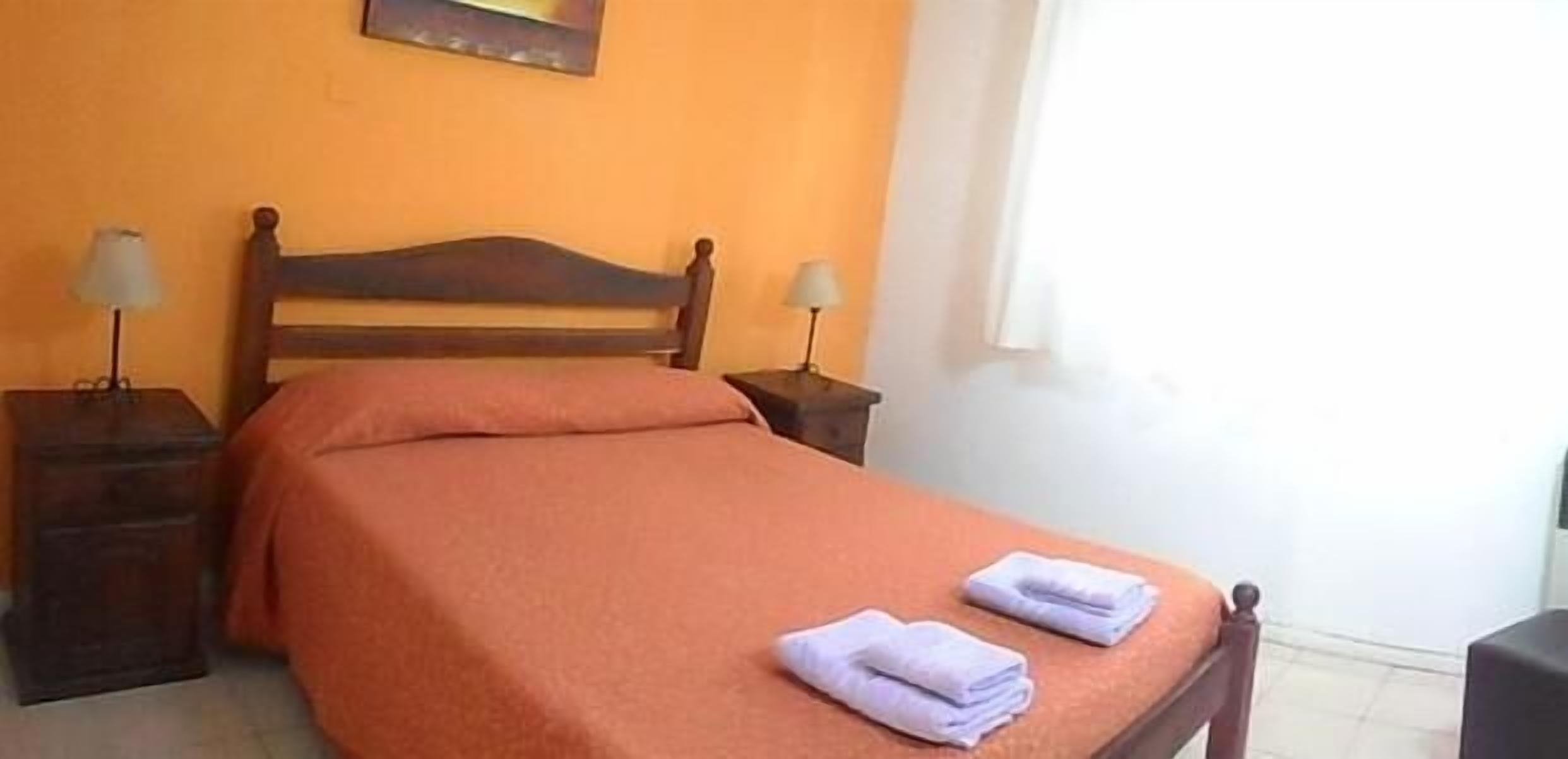 A single bed with a wooden headboard, two bedside tables with lamps, and a window with curtains.