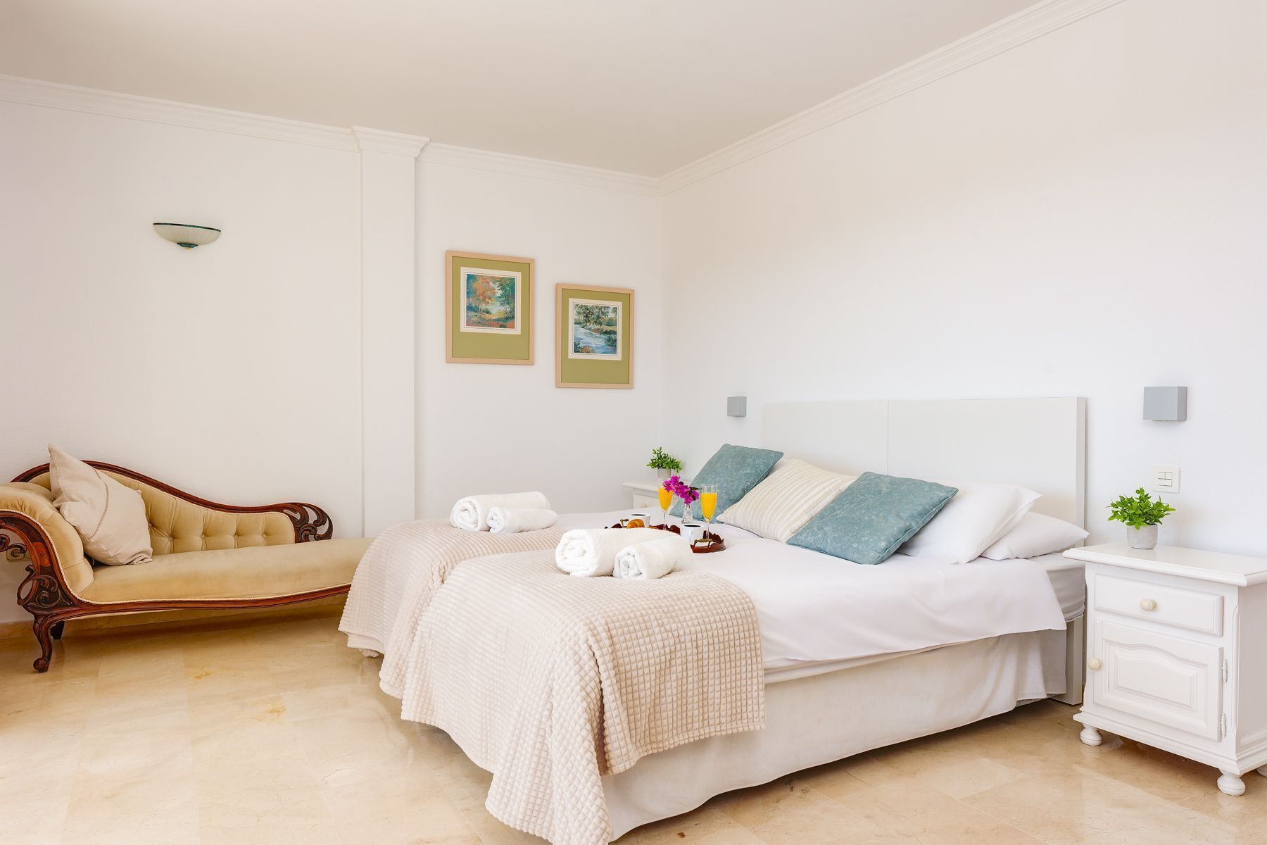 Une chambre d’hôtel avec un lit, un canapé, une table de chevet et deux tableaux encadrés au mur.