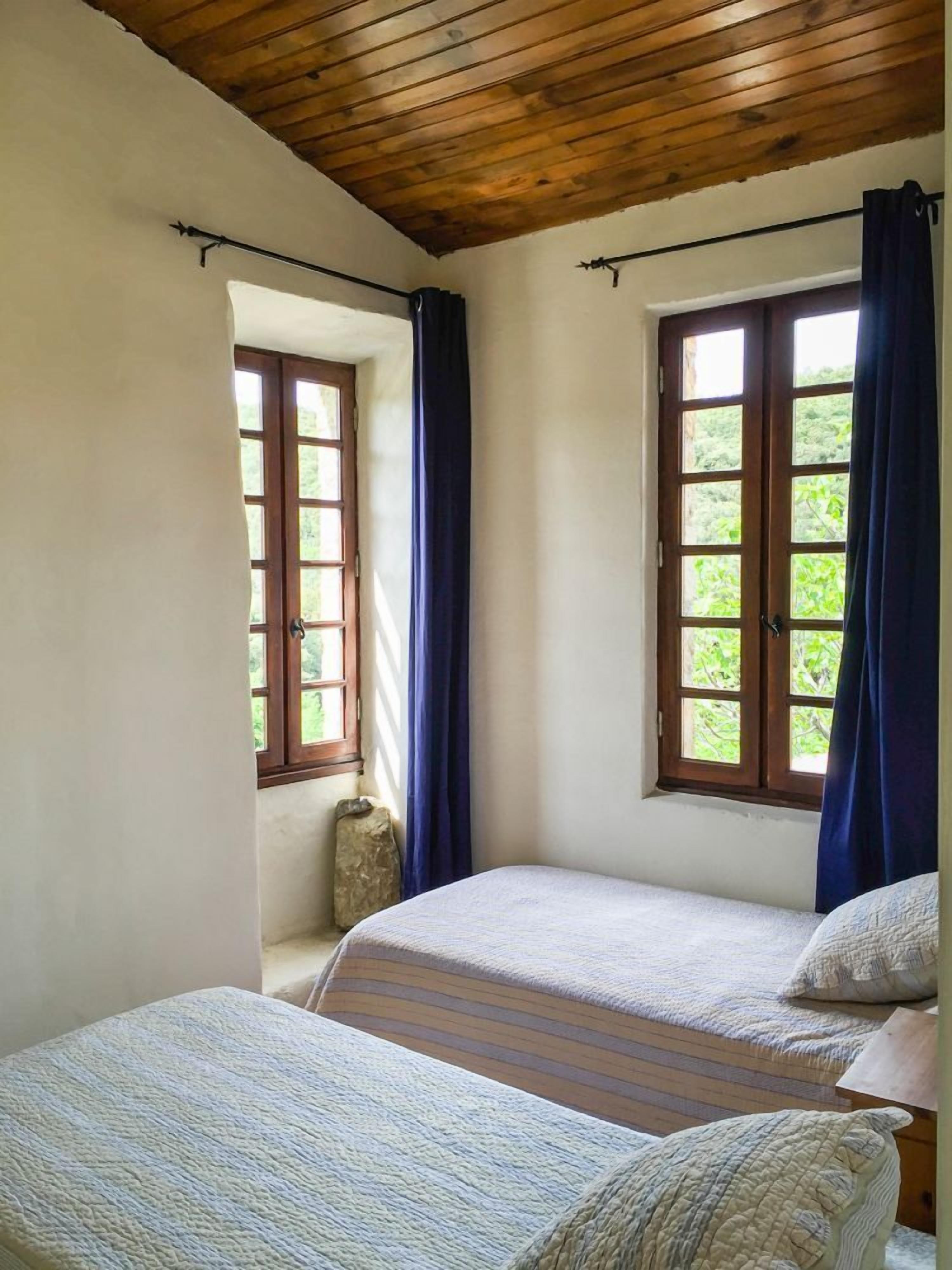 Ein Schlafzimmer mit zwei Betten, Holzboden und Fenstern mit Vorhängen.