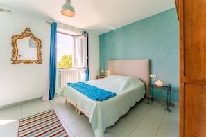 A bedroom with a bed, a window with curtains, a bedside table, and a wall-mounted mirror. - Apartment 'Côté Vigne' with Shared Pool, Private Terrace and Wi-Fi (Rasteau)