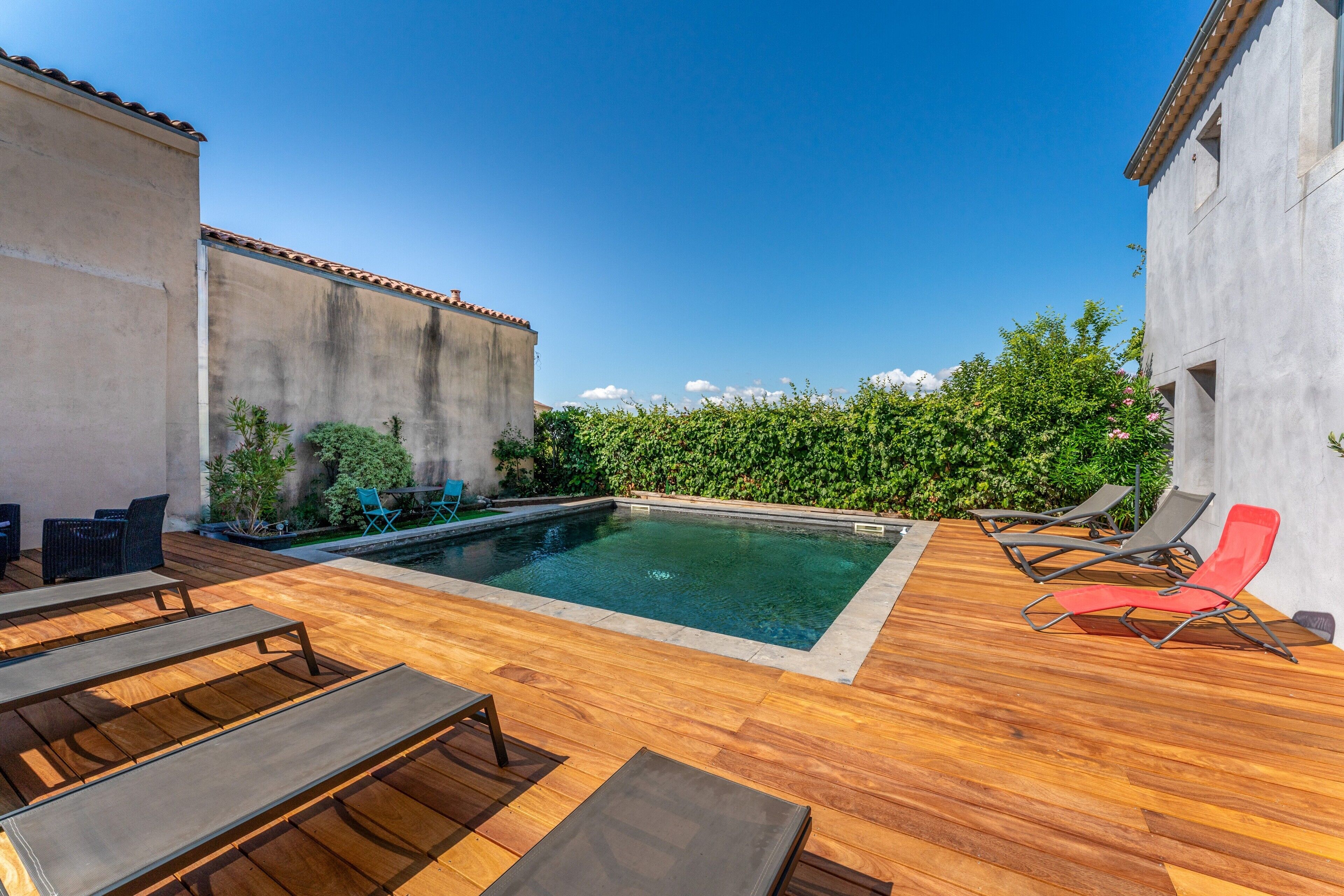A swimming pool with lounge chairs, a wooden deck, and a hedge.