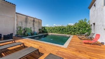 A swimming pool with lounge chairs, a wooden deck, and a hedge.