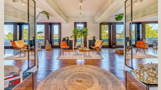 A spacious living area with a large wooden floor, a central rug, and multiple seating areas with orange chairs. - Skylife Peacock Penthouse (Roma)