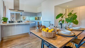 A modern kitchen with a central island, a dining area with a wooden table, and a large plant. - Skylife Peacock Penthouse (Roma)