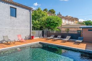 Una piscina con lettini, un pontile in legno e un edificio con tetto in tegole.