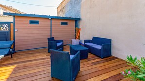 Une terrasse extérieure avec des meubles en osier, une plateforme en bois et un portail en métal.
