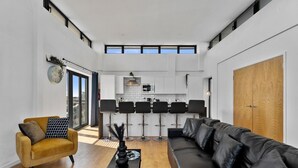 Un salon moderne avec un canapé, un fauteuil jaune et une table basse. On y trouve également un coin cuisine avec un ensemble de salle à manger et une grande porte en bois.