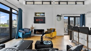 Un salon moderne avec une cheminée, un canapé bleu, un fauteuil jaune et un coin bar avec des tabourets.
