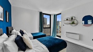 Une chambre d’h ôtel moderne comprenant un lit, deux tables de chevet, une fenêtre avec des rideaux, un radiateur et des œuvres d’art murales.