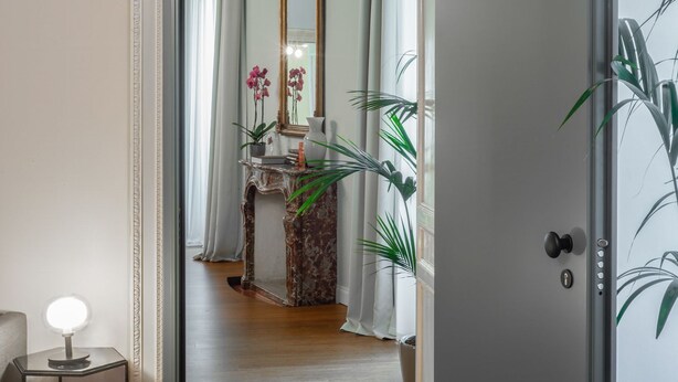 Un couloir avec une console en marbre, un miroir et des plantes en pot.