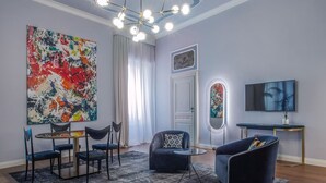 Una sala de estar moderna con un cuadro abstracto grande, un comedor con sillas, un sofá y un televisor en la pared.