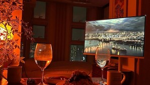 Une table à manger avec un saladier rempli de nourriture, deux verres à vin et un téléviseur diffusant une vue sur une ville.