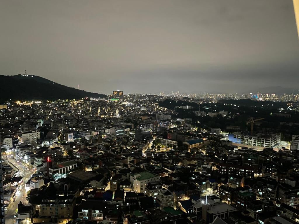 A nighttime cityscape with dense urban buildings and a distant hill.