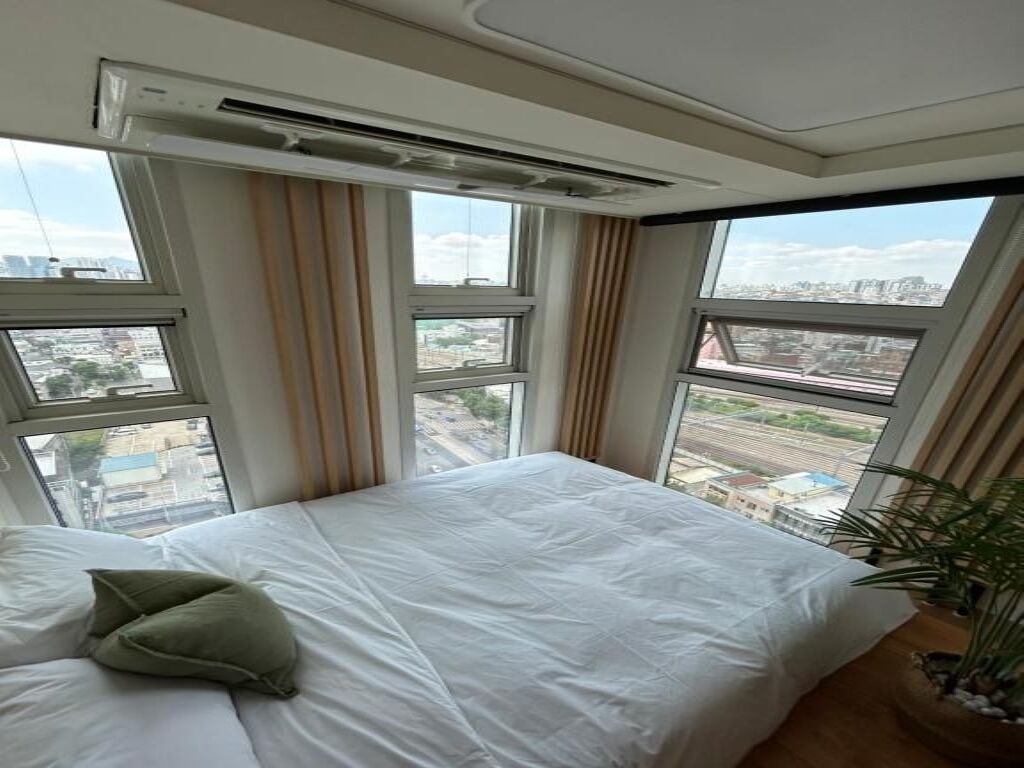 A hotel room with a large bed, an air conditioning unit, and a view of the city through large windows.