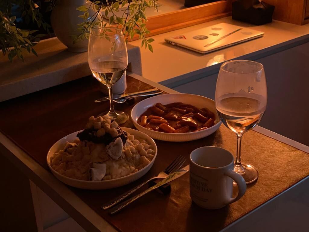 A dining table with a plate of food, a bowl of pasta, and two glasses of white wine.
