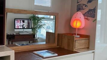 A room with a desk, a computer monitor, a plant, a window with a view, and a wall with fish illustrations.