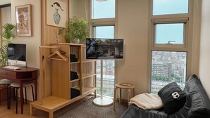 Een moderne woonkamer met een zwarte leren bank, een houten boekenkast, een bureau met een computer en een televisie.