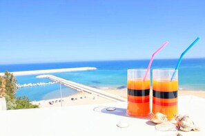 Two glasses of orange juice with black and red stripes, a pier, and the ocean in the background.
