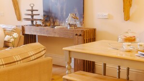 Una sala de estar acogedora con una mesa de madera, un banco y un sofá. Hay una pieza decorativa sobre la mesa y un florero con flores en el sofá.