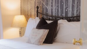 Una cama bien hecha con sábanas blancas, un cojín decorativo con texto y una lámpara sobre una mesita de noche.