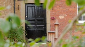 A black door with a small wooden gate to the right, a brick wall, and a sign that reads "Game Cottage." - Game Cottage (Bridgnorth)