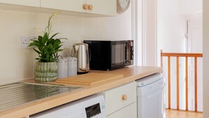 A kitchen with white cabinets, a microwave, a coffee maker, and a dishwasher. - Game Cottage (Bridgnorth)