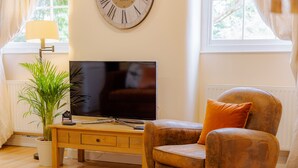 A living room with a wooden coffee table, a television, a leather armchair, and a potted plant. - Coachmans Cottage (Bridgnorth)
