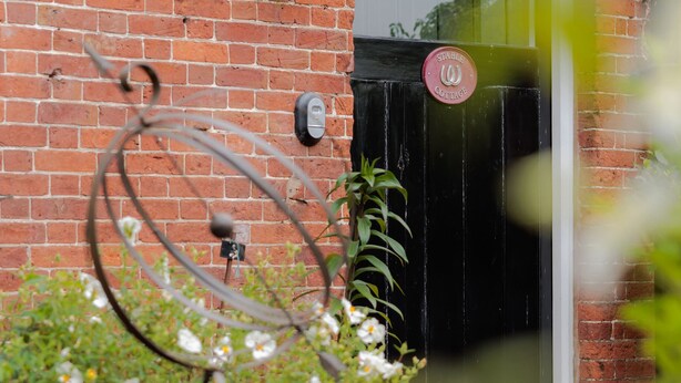 A brick wall with a black door, a metal sculpture, and a sign that reads "Stable Cottage". - Stable Cottage (Bridgnorth)