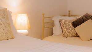 A bed with a quilted white duvet, a patterned pillow, and a plain pillow. A bedside lamp with a beige shade is on the left. - Stable Cottage (Bridgnorth)