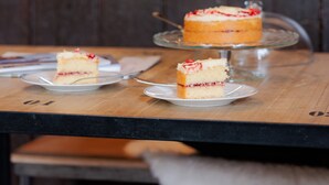 A wooden table with a cake on a glass stand and a slice on a plate. - Stable Cottage (Bridgnorth)