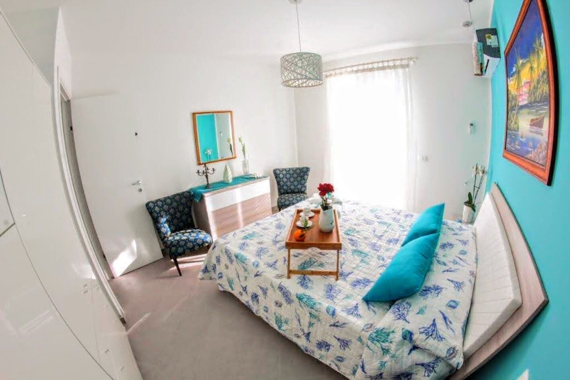 A bedroom with a bed, a dresser, a chair, a hanging light fixture, and a painting on the wall.