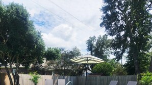 Een rechthoekig zwembad met helderblauw water, omgeven door een terras met een kiezelstructuur. Er staan twee ligbedden en een parasol voor schaduw.